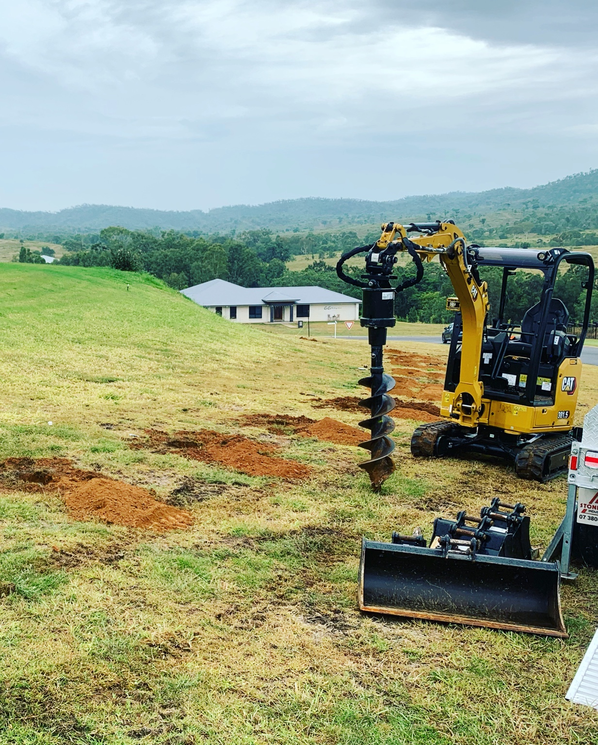 Mini excavator augering post holes across a rural property